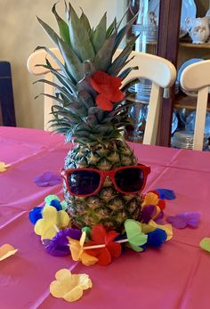 a pineapple wearing sunglasses on a pink table cloth with flowers and streamers around it