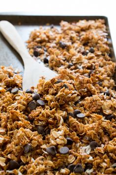 granola in a pan with a wooden spoon on the side and chocolate chips scattered around it