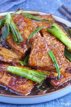 tofu and asparagus in sauce on a plate with chopsticks next to it