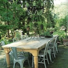 a wooden table surrounded by chairs and potted plants in a backyard area with lots of greenery