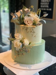 two tiered wedding cake with white flowers and greenery on the top, sitting on a plate