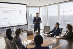 a group of business people sitting around a conference table in front of large panoramic windows