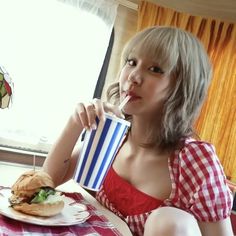 a woman sitting at a table with a sandwich and drink