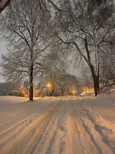 a snow covered road with trees and street lights in the distance at night, on a snowy day