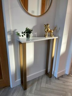 a small white table with a mirror on the wall above it and a plant in a vase next to it