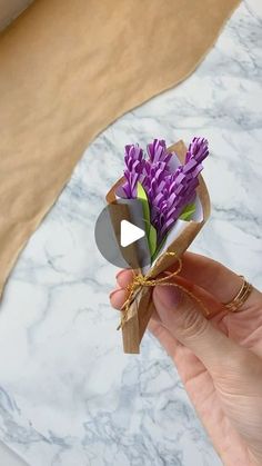 someone is holding a small purple flower in front of a white marble counter top with a video about how to make it