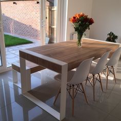 a wooden table with white chairs and flowers in a vase on the top of it