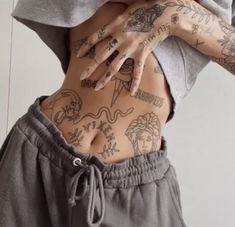 a woman with tattoos on her stomach wearing sweatpants and holding her hands behind her back