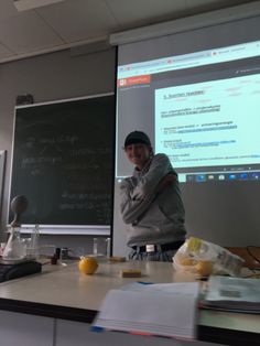 a man standing in front of a projector screen next to a desk with lemons on it