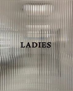 the words ladies are etched on an aluminum plated glass wall with wavy lines and black lettering