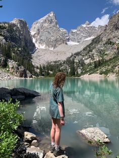 a woman standing on top of a rock next to a lake with mountains in the background