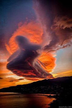 an unusual cloud formation is seen in the sky at sunset over water and land, with mountains in the background