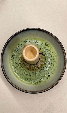 a green and black dish with a brush in the center on a white tablecloth