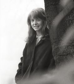 a black and white photo of a woman leaning against a tree