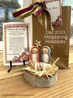 two wooden dolls sitting on top of a table next to a sign and gift bag