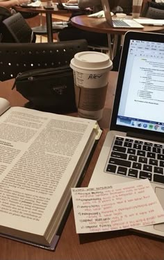 an open book sitting on top of a table next to a laptop computer and cup of coffee