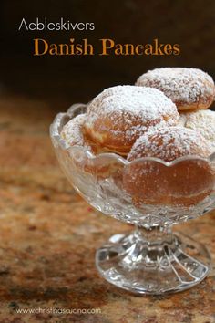 some powdered sugar covered doughnuts in a glass bowl on a counter top