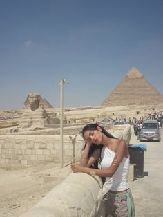 a woman leaning on a wall in front of the pyramids