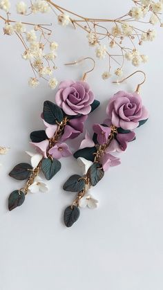 two pink roses and leaves are hanging from the stems of some white flowers on a branch