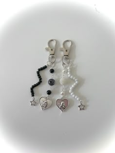 three charms are hanging on a white surface with black beads and silver heart shaped pendants