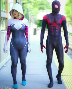 two people in spider - man costumes are walking down the sidewalk