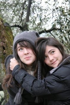 two young women hugging each other in front of a tree with no leaves on it