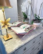 a table with a lamp, books and flowers on it in front of a mirror