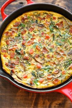 an omelet with sausage, spinach and cheese in a red pan on a wooden table