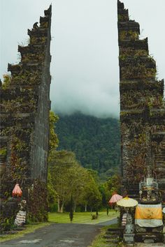 two stone archways with umbrellas in front of them on a road near mountains