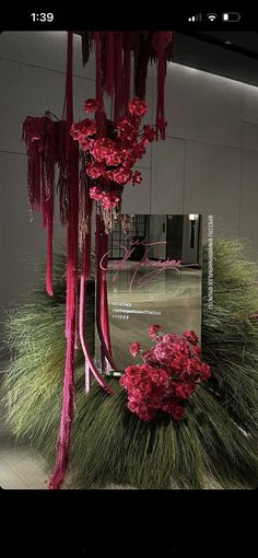 red flowers and grass in front of a large mirror with pink ribbons hanging from it