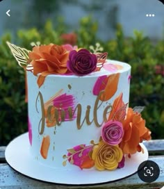 a decorated cake sitting on top of a wooden table next to flowers and greenery