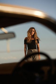 a woman standing in front of a car looking at the camera with her hand on her hip