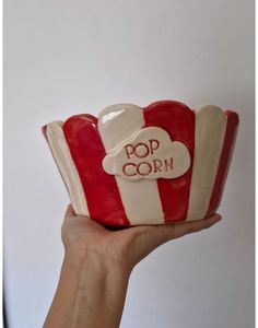 a hand holding a red and white striped cup with the word pop corn on it