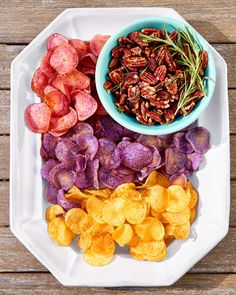 a white plate topped with lots of different types of chips next to a blue bowl filled with dried fruit