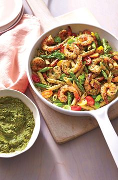 a pan filled with shrimp and veggies next to a bowl of pesto sauce