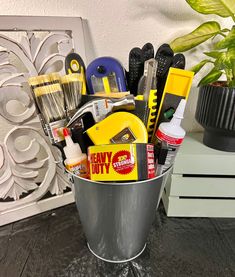 a metal bucket filled with cleaning supplies on top of a table next to a potted plant