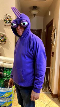 a man in a purple costume standing next to a pile of bottled water and looking at the camera