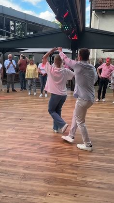 two people dancing on a wooden floor in front of a group of people standing around