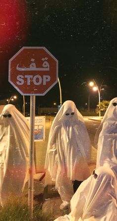 three people dressed in white cloths standing next to a stop sign with ghost covering them