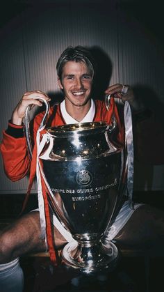 a man sitting on the ground holding up a soccer trophy in front of his face