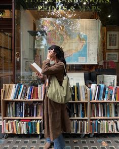 a woman standing in front of a book store talking on her cell phone while holding a book