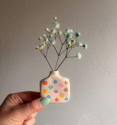 a hand holding a small ceramic vase with flowers in it's top and bottom