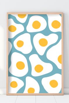 an egg print is hanging on the wall in front of a white background with blue and yellow eggs