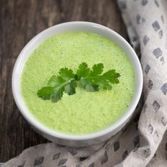 a white bowl filled with green soup and garnished with parsley on top