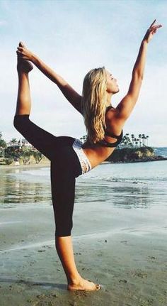 a woman doing yoga on the beach with her arms in the air and one leg up