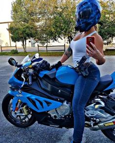 a woman sitting on a blue motorcycle looking at her cell phone while wearing a helmet