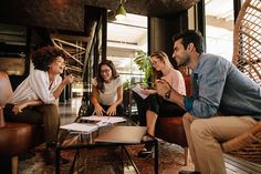 a group of people sitting around a coffee table in a living room looking at papers