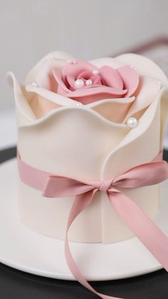 a pink rose on top of a white cake with pearls and ribbon tied around it