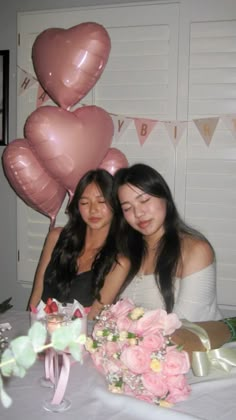 two women sitting at a table with pink flowers and balloons in the shape of hearts