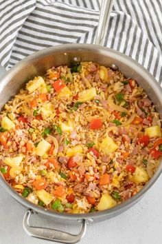 a pan filled with rice and vegetables on top of a table next to a striped towel